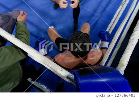 Top view of cornered boxer receives strategic advice from trainer during intense bout. 127566403