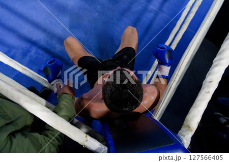 Top view of cornered boxer receives strategic advice from trainer during intense bout. 127566405