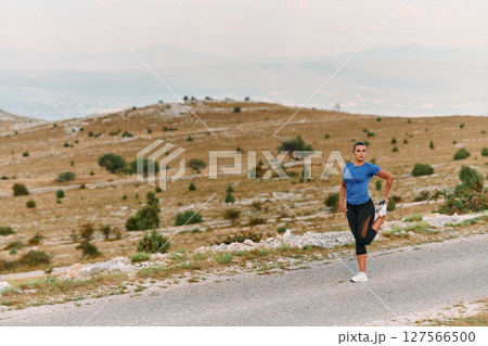 Determined Female Athlete Stretching After an Intense Run Through Rugged Mountain Terrain. 127566500