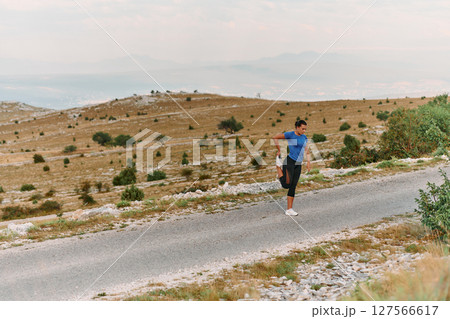 Determined Female Athlete Stretching After an Intense Run Through Rugged Mountain Terrain. Determined Female Athlete Stretching After an Intense Run Through Rugged Mountain Terrain. 127566617