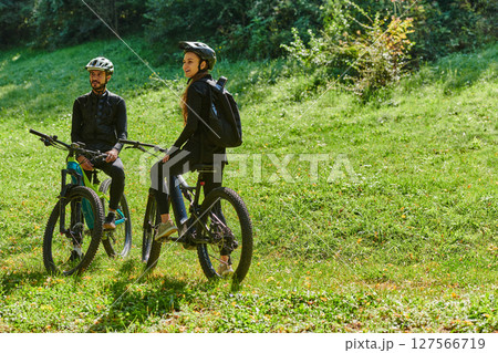 A blissful couple, adorned in professional cycling gear, enjoys a romantic bicycle ride through a park, surrounded by modern natural attractions, radiating love and happiness 127566719