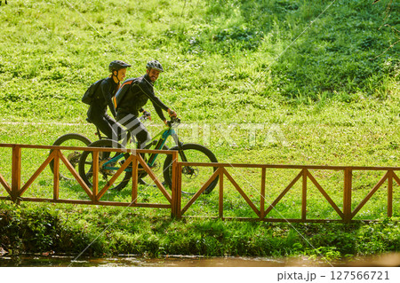 A blissful couple, adorned in professional cycling gear, enjoys a romantic bicycle ride through a park, surrounded by modern natural attractions, radiating love and happiness 127566721