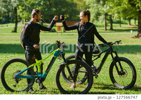 A sweet couple, adorned in cycling gear, rides their bicycles, their hands interlocked in a romantic embrace, capturing the essence of love, adventure, and joy on a sunlit path 127566747