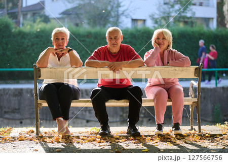 A group of elderly individuals, including a senior man and two older women, sits in a park on a sunny autumn day, embodying the concept of healthy aging through companionship, relaxation, and outdoor 127566756