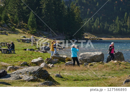 A family shares delightful moments with their friends amid the stunning landscapes of mountains, lakes, and winding paths, promoting a healthy lifestyle and the joy of familial bonds in the embrace of 127566893