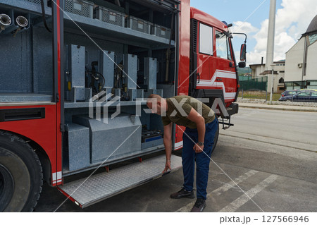 A dedicated firefighter preparing a modern firetruck for deployment to hazardous fire-stricken areas, demonstrating readiness and commitment to emergency response A dedicated firefighter preparing a modern firetruck for deployment to hazardous fire-stricken areas, demonstrating readiness and commitment to emergency response 127566946