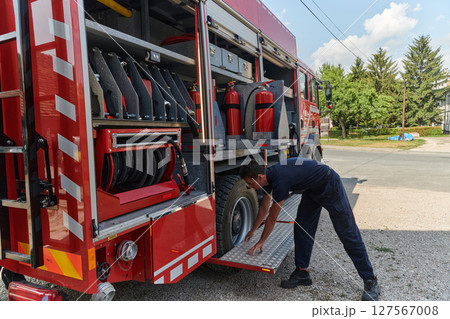 A dedicated firefighter preparing a modern firetruck for deployment to hazardous fire-stricken areas, demonstrating readiness and commitment to emergency response A dedicated firefighter preparing a modern firetruck for deployment to hazardous fire-stricken areas, demonstrating readiness and commitment to emergency response 127567008