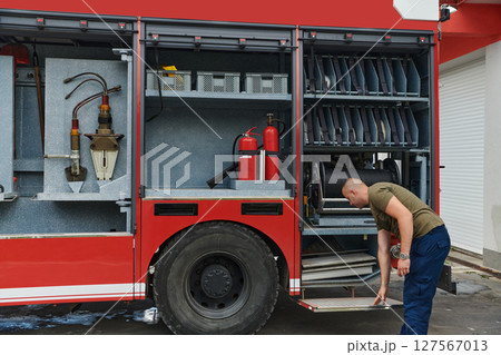 A dedicated firefighter preparing a modern firetruck for deployment to hazardous fire-stricken areas, demonstrating readiness and commitment to emergency response A dedicated firefighter preparing a modern firetruck for deployment to hazardous fire-stricken areas, demonstrating readiness and commitment to emergency response 127567013