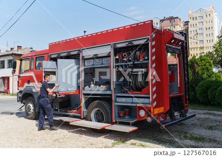 A dedicated firefighter preparing a modern firetruck for deployment to hazardous fire-stricken areas, demonstrating readiness and commitment to emergency response A dedicated firefighter preparing a modern firetruck for deployment to hazardous fire-stricken areas, demonstrating readiness and commitment to emergency response 127567016