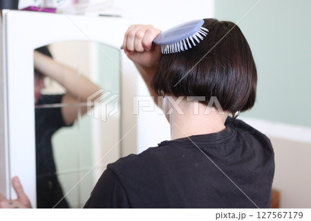 Woman brushing her bob haircut in front of mirror Woman brushing her bob haircut in front of mirror 127567179