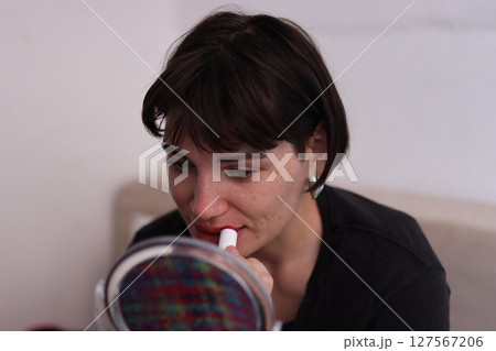Young woman applying red lipstick while looking in mirror Young woman applying red lipstick while looking in mirror 127567206