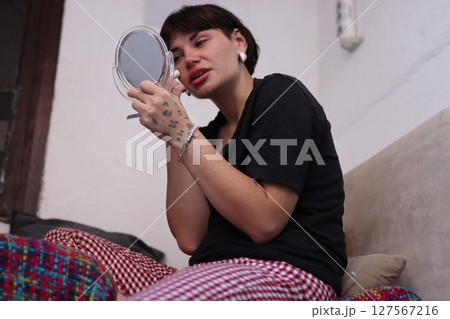 Young woman applying makeup while looking in a handheld mirror at home Young woman applying makeup while looking in a handheld mirror at home 127567216