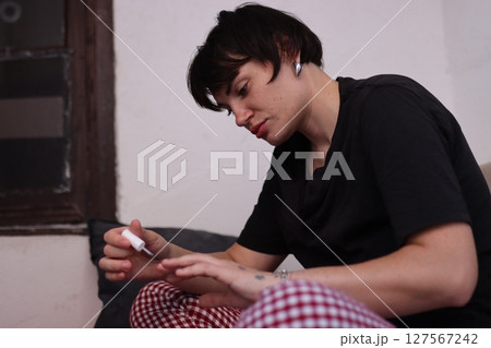 Young woman applying nail polish on sofa at home 127567242