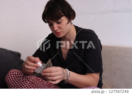 Young woman applying nail polish on sofa at home Young woman applying nail polish on sofa at home 127567248