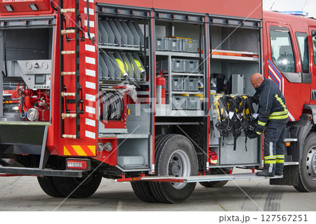 A firefighter meticulously prepares a modern firetruck for a mission to evacuate and respond to dangerous situations, showcasing the utmost dedication to safety and readiness in the face of a fire 127567251