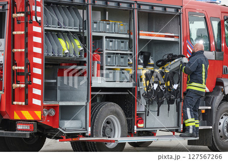 A firefighter meticulously prepares a modern firetruck for a mission to evacuate and respond to dangerous situations, showcasing the utmost dedication to safety and readiness in the face of a fire A firefighter meticulously prepares a modern firetruck for a mission to evacuate and respond to dangerous situations, showcasing the utmost dedication to safety and readiness in the face of a fire 127567266