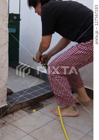 Woman watering plants on balcony with yellow hose 127567283