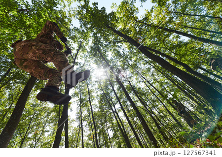 An elite soldier adeptly clears military barriers in the perilous wooded terrain, showcasing tactical skill and agility during specialized training An elite soldier adeptly clears military barriers in the perilous wooded terrain, showcasing tactical skill and agility during specialized training 127567341