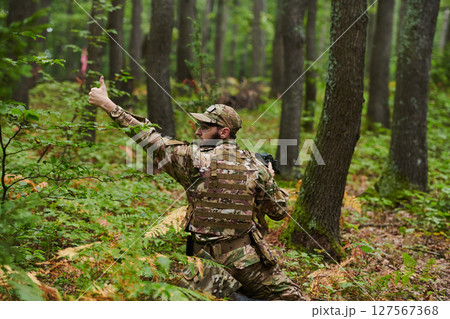An elite soldier, camouflaged and stealthily navigating through dangerous woodland terrain, executes a covert mission in a secluded forest area An elite soldier, camouflaged and stealthily navigating through dangerous woodland terrain, executes a covert mission in a secluded forest area 127567368
