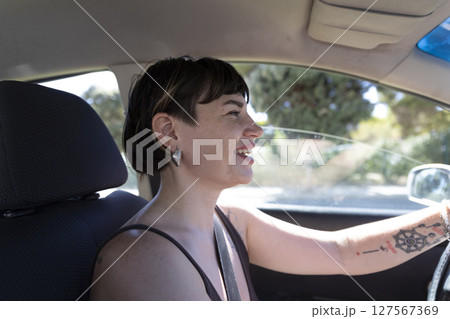 Young woman driving car and smiling during summer day Young woman driving car and smiling during summer day 127567369