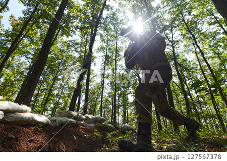 An elite soldier adeptly clears military barriers in the perilous wooded terrain, showcasing tactical skill and agility during specialized training An elite soldier adeptly clears military barriers in the perilous wooded terrain, showcasing tactical skill and agility during specialized training 127567378