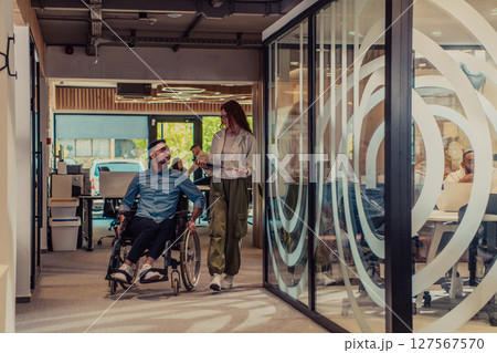 Young business colleagues, collaborative business colleagues, including a person in a wheelchair, walk past a modern glass office corridor, illustrating diversity, teamwork and empowerment in the Young business colleagues, collaborative business colleagues, including a person in a wheelchair, walk past a modern glass office corridor, illustrating diversity, teamwork and empowerment in the 127567570