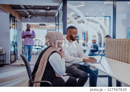 In a modern office setting, an African American businessman and his Muslim colleague, wearing a hijab, engage in collaborative discussions, tackling various business tasks and solving problems In a modern office setting, an African American businessman and his Muslim colleague, wearing a hijab, engage in collaborative discussions, tackling various business tasks and solving problems 127567620