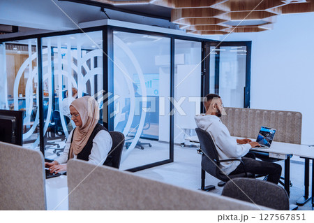 In a modern office setting, an African American businessman and his Muslim colleague, wearing a hijab, engage in collaborative discussions, tackling various business tasks and solving problems 127567851