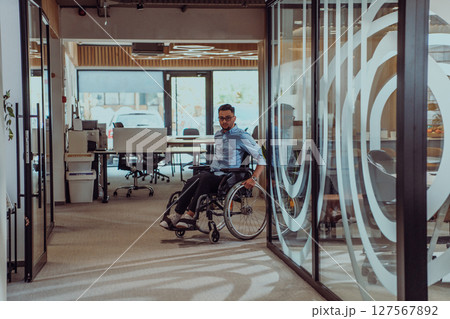 In a large modern corporation, a determined businessman in a wheelchair navigates through a hallway, embodying empowerment and inclusivity in the corporate world. 127567892