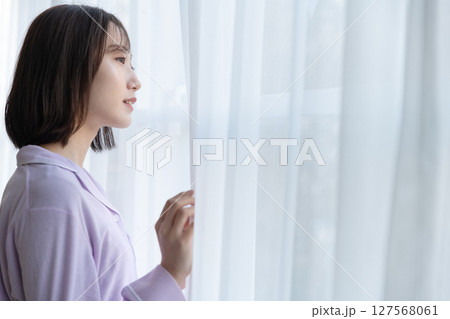 レースのカーテンの隙間からで外を見ている若い女性 レースのカーテンの隙間からで外を見ている若い女性 127568061