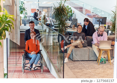 A company director assists his business colleague in a wheelchair, helping her navigate to their startup office, where they work alongside their diverse team of colleagues, emphasizing inclusivity and A company director assists his business colleague in a wheelchair, helping her navigate to their startup office, where they work alongside their diverse team of colleagues, emphasizing inclusivity and 127568137