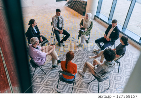 Top view of a diverse group of young business entrepreneurs gathered in a circle for a meeting, discussing corporate challenges and innovative solutions within the modern confines of a large Top view of a diverse group of young business entrepreneurs gathered in a circle for a meeting, discussing corporate challenges and innovative solutions within the modern confines of a large 127568157