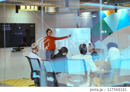 A pregnant business woman with orange hair confidently presents her business plan to colleagues in a modern glass office, embodying entrepreneurship and innovation 127568181