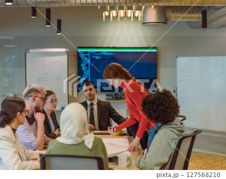 A diverse team of business experts in a modern glass office, attentively listening to a colleague's presentation, fostering collaboration and innovation A diverse team of business experts in a modern glass office, attentively listening to a colleague's presentation, fostering collaboration and innovation 127568210