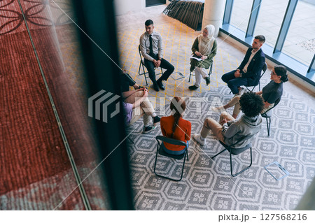 Top view of a diverse group of young business entrepreneurs gathered in a circle for a meeting, discussing corporate challenges and innovative solutions within the modern confines of a large Top view of a diverse group of young business entrepreneurs gathered in a circle for a meeting, discussing corporate challenges and innovative solutions within the modern confines of a large 127568216
