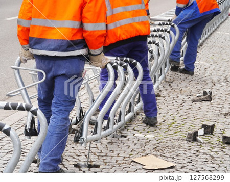 Three men in orange and blue safety gear are working on a metal fence Three men in orange and blue safety gear are working on a metal fence 127568299
