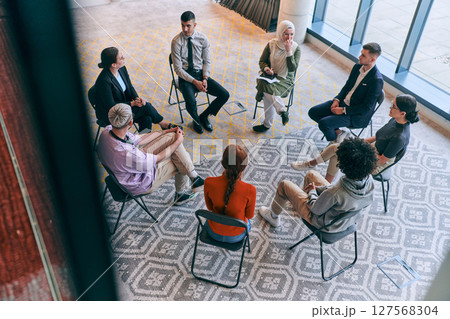 Top view of a diverse group of young business entrepreneurs gathered in a circle for a meeting, discussing corporate challenges and innovative solutions within the modern confines of a large 127568304
