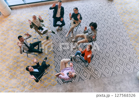 Top view of a diverse group of young business entrepreneurs gathered in a circle for a meeting, discussing corporate challenges and innovative solutions within the modern confines of a large 127568326
