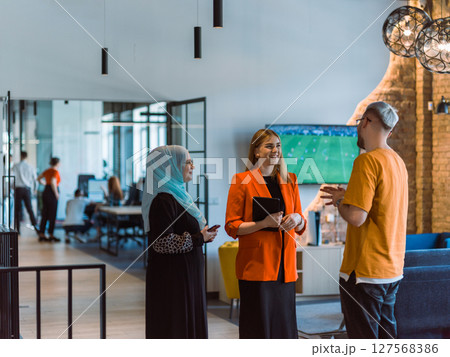 A group of young business colleagues, including a woman in a hijab, stands united in the modern corridor of a spacious startup coworking center, representing diversity and collaborative spirit 127568386