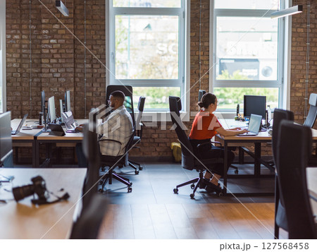 A diverse group of young business individuals congregates in a modern startup coworking center, embodying collaborative innovation and a dynamic atmosphere 127568458