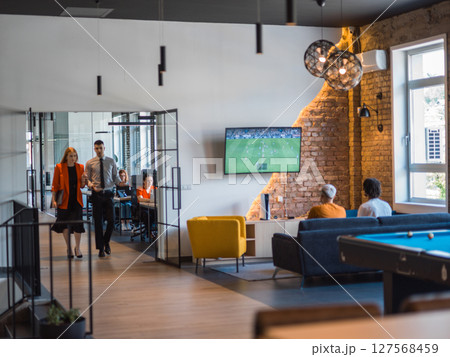 A business group, including an African American businessman in a wheelchair, collaborates within a modern glass office, actively engaged around a computer and laptop, collectively solving diverse 127568459