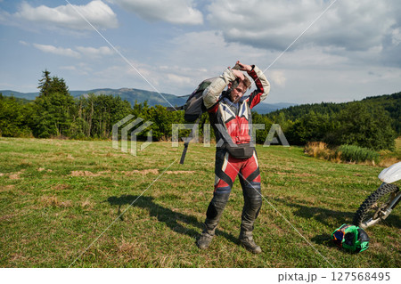 A professional motocross rider, clad in a full suit, gloves, and backpack, prepares for a daring adventure through the forest, geared up for an adrenaline-pumping off-road journey 127568495