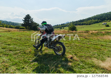 A motorcyclist equipped with professional gear, rides motocross on perilous meadows, training for an upcoming competition. 127568546