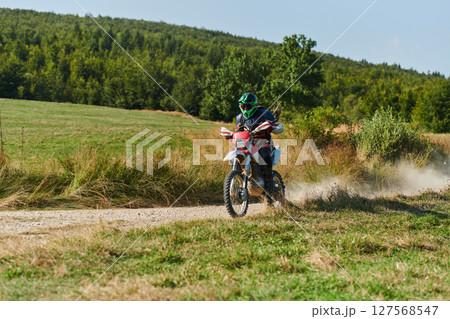 A professional motocross rider exhilaratingly riding a treacherous off-road forest trail on their motorcycle. 127568547