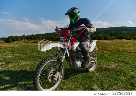 A motorcyclist equipped with professional gear, rides motocross on perilous meadows, training for an upcoming competition. 127568557
