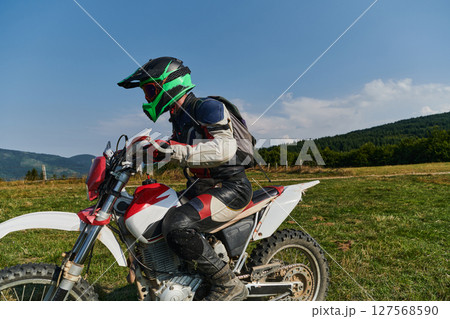 A motorcyclist equipped with professional gear, rides motocross on perilous meadows, training for an upcoming competition. 127568590