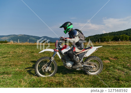 A motorcyclist equipped with professional gear, rides motocross on perilous meadows, training for an upcoming competition. A motorcyclist equipped with professional gear, rides motocross on perilous meadows, training for an upcoming competition. 127568592