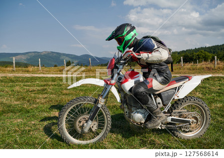 A motorcyclist equipped with professional gear, rides motocross on perilous meadows, training for an upcoming competition. 127568614