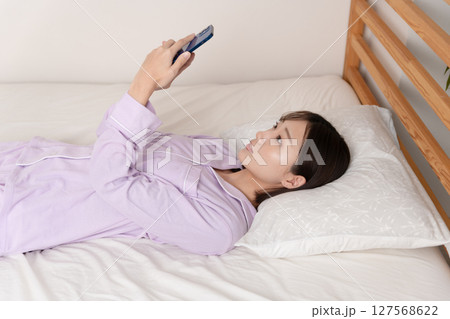 ベッドで寝たままスマホを操作する若い女性 127568622