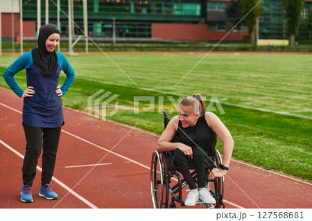 A Muslim woman in a burqa running together with a woman in a wheelchair on the marathon course, preparing for future competitions. 127568681